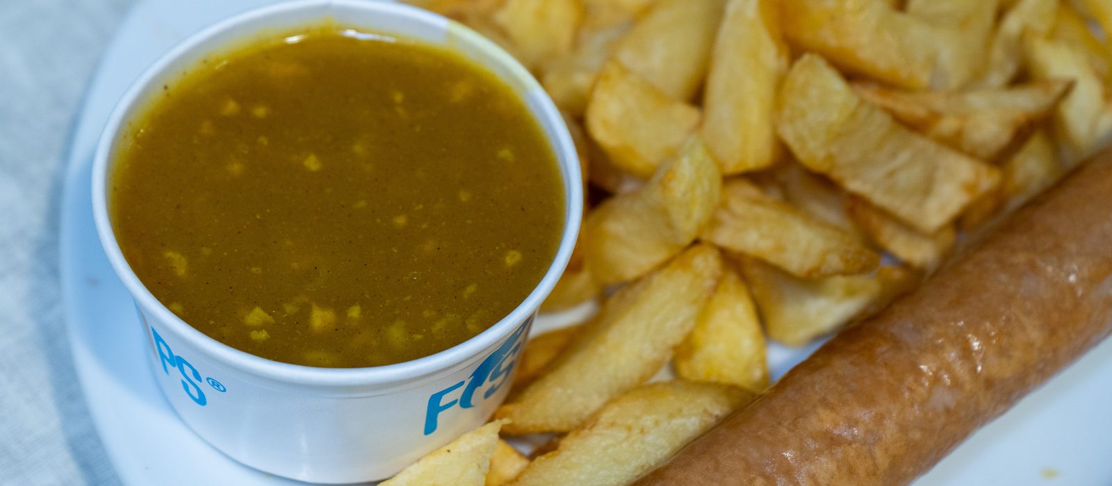 Chips with a pot of curry sauce and a battered sausage